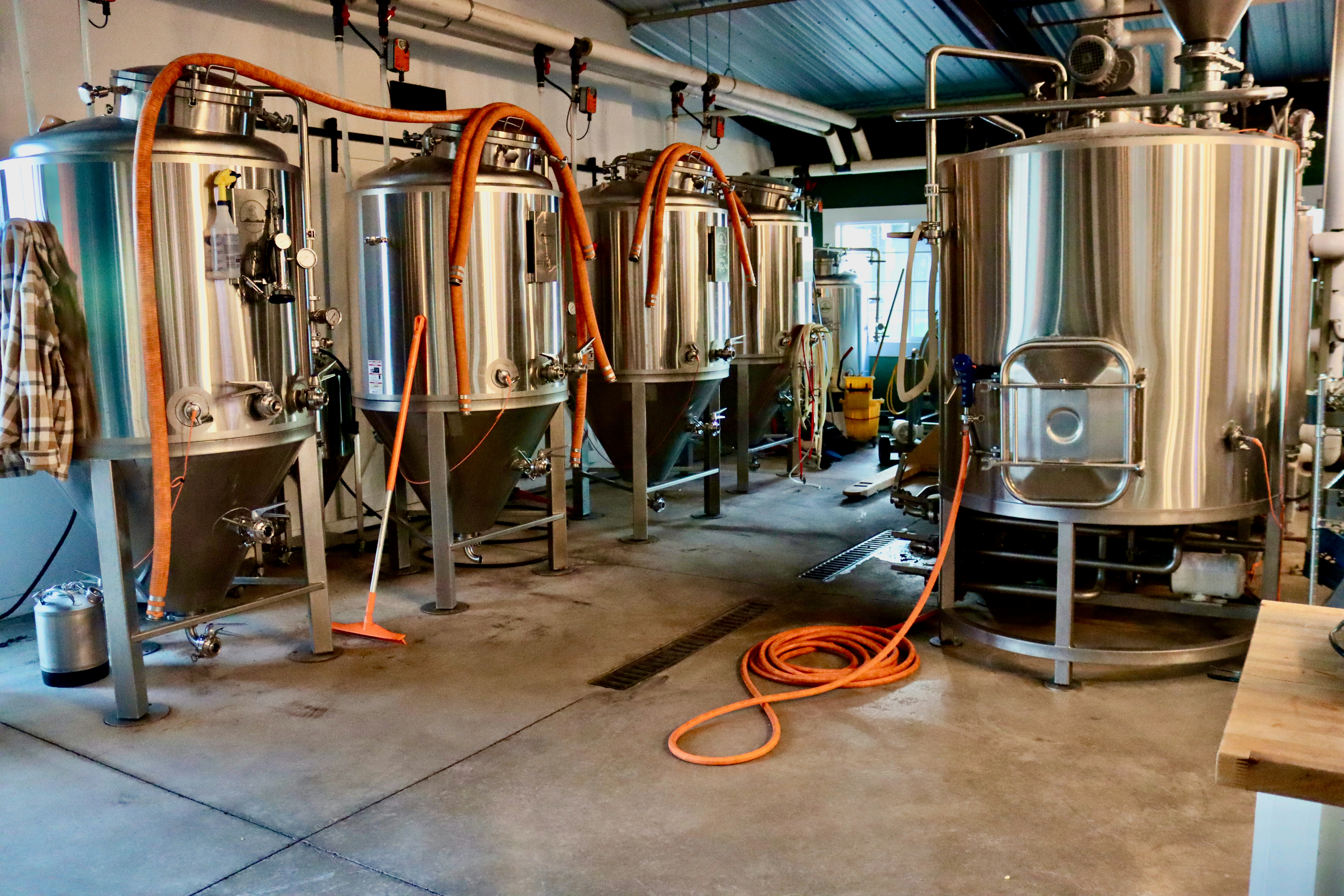 Craft brewery interior with four stainless steel fermentation tanks and glycol hoses